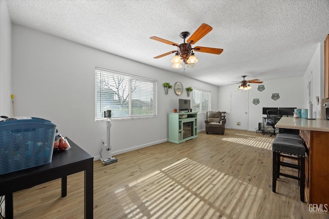 living room with baseboards, ceiling fan, a textured ceiling, and light wood finished floors