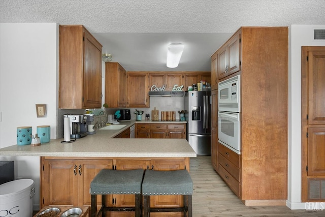 kitchen with light countertops, a sink, light wood-type flooring, white appliances, and a peninsula