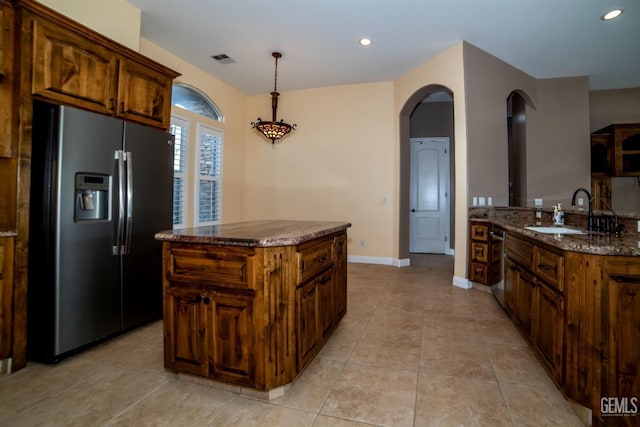 kitchen with sink, dark stone counters, hanging light fixtures, a center island, and stainless steel refrigerator with ice dispenser