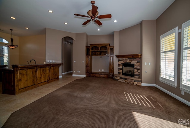 unfurnished living room with light tile patterned flooring, a stone fireplace, a healthy amount of sunlight, and ceiling fan