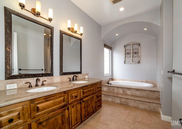 bathroom with a relaxing tiled tub, vanity, and tile patterned flooring