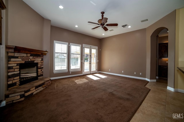 unfurnished living room with tile patterned flooring, a stone fireplace, and ceiling fan