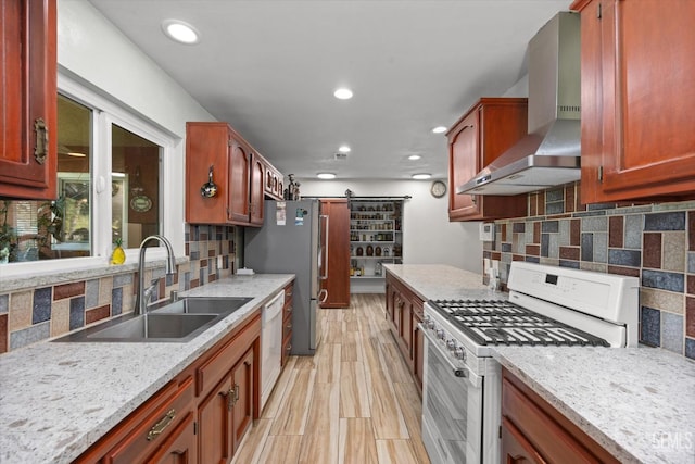 kitchen with white appliances, sink, wall chimney exhaust hood, a barn door, and light stone countertops