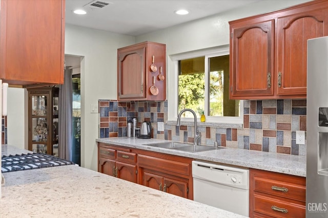 kitchen featuring light stone countertops, sink, backsplash, stainless steel fridge, and white dishwasher