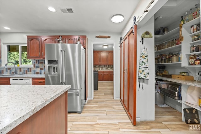 kitchen with stainless steel refrigerator with ice dispenser, tasteful backsplash, white dishwasher, sink, and a barn door