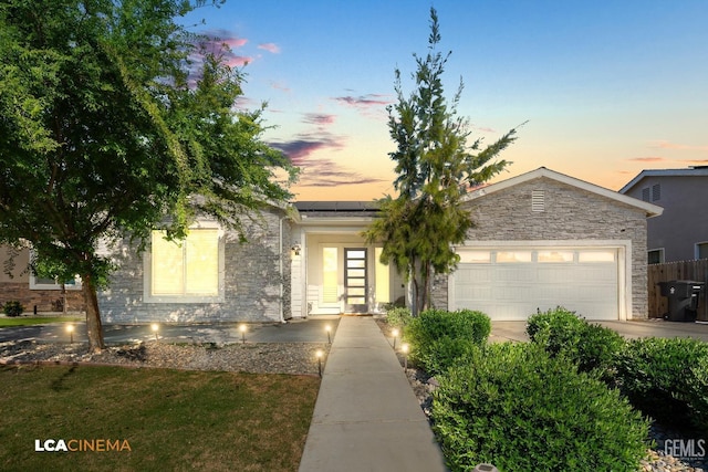 view of front of home featuring concrete driveway, roof mounted solar panels, stone siding, and a garage