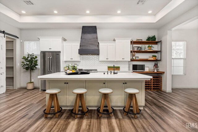 kitchen with a center island with sink, a barn door, white cabinets, custom exhaust hood, and high end fridge