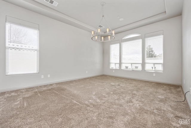 carpeted empty room featuring visible vents, a raised ceiling, a notable chandelier, and baseboards