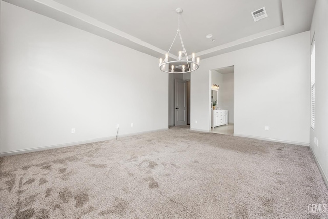 carpeted empty room with a tray ceiling, baseboards, visible vents, and an inviting chandelier