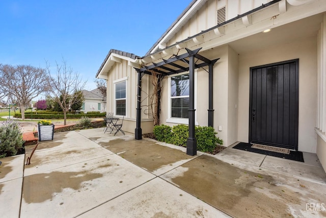 entrance to property with a patio area, stucco siding, board and batten siding, and a pergola