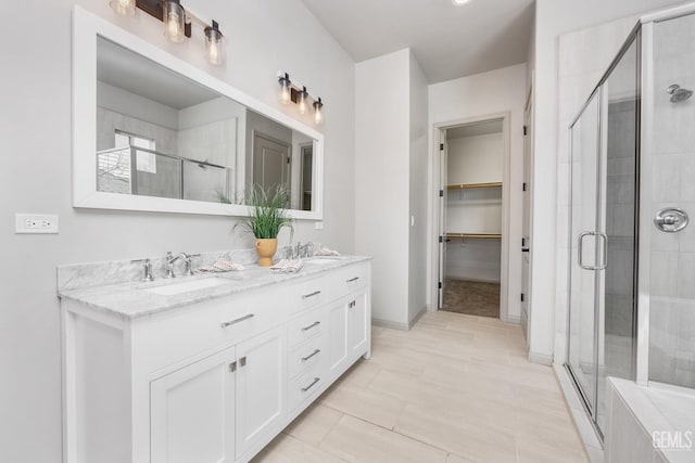 bathroom featuring double vanity, a shower stall, a walk in closet, and a sink