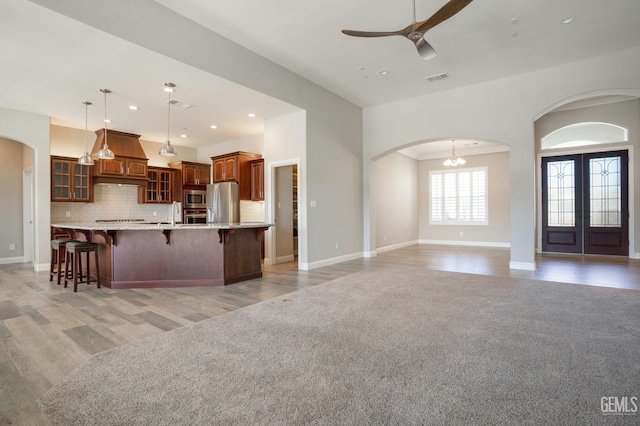 kitchen featuring glass insert cabinets, a breakfast bar, ceiling fan with notable chandelier, arched walkways, and stainless steel appliances