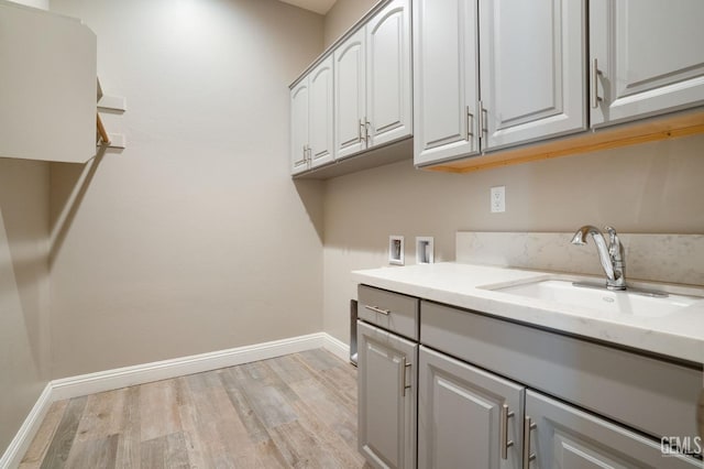 washroom with hookup for a washing machine, baseboards, cabinet space, a sink, and light wood-style floors