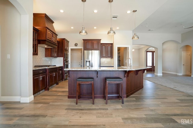 kitchen with visible vents, a breakfast bar, light wood-style flooring, arched walkways, and appliances with stainless steel finishes