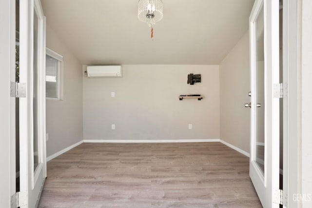 empty room featuring baseboards, lofted ceiling, an AC wall unit, and light wood-style flooring