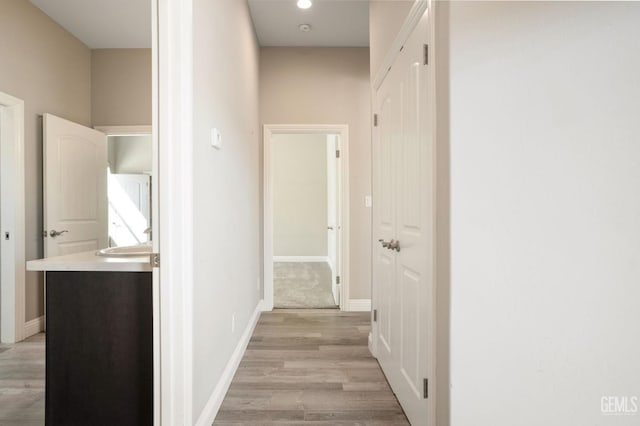 hallway featuring baseboards, light wood finished floors, and a sink