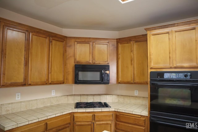 kitchen featuring brown cabinets, black appliances, and tile counters