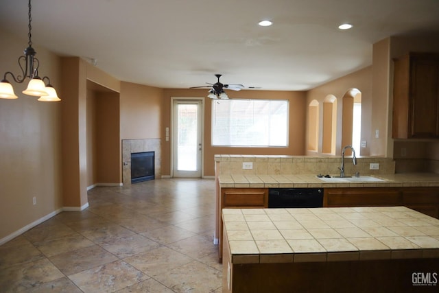 kitchen featuring a tiled fireplace, tile countertops, dishwasher, a peninsula, and a sink