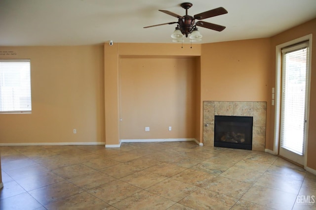 unfurnished living room with a tiled fireplace, a ceiling fan, and baseboards