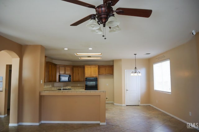 kitchen with black appliances, arched walkways, a peninsula, brown cabinetry, and baseboards