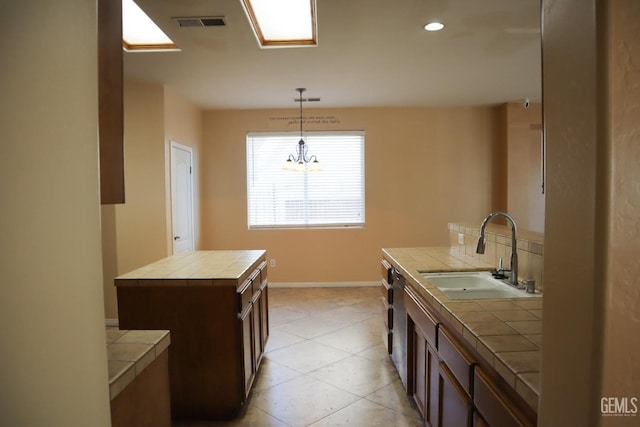 kitchen with a sink, tile countertops, baseboards, dark brown cabinets, and hanging light fixtures