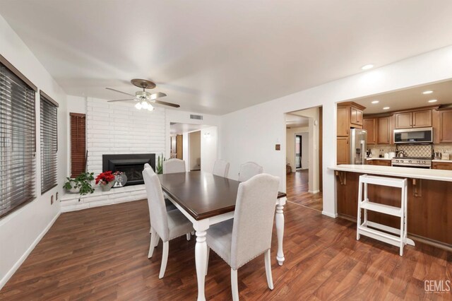 dining room featuring ceiling fan, dark hardwood / wood-style floors, and a brick fireplace