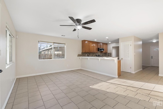 kitchen featuring light tile patterned floors, a peninsula, a breakfast bar, tasteful backsplash, and stainless steel microwave