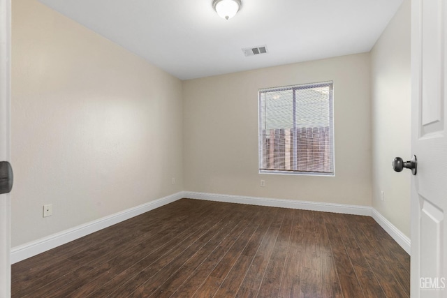 empty room with dark wood-type flooring, visible vents, and baseboards