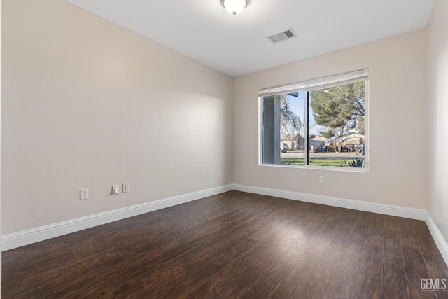 empty room featuring baseboards, visible vents, and dark wood finished floors