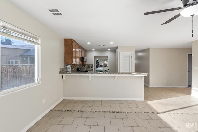 kitchen with baseboards, visible vents, decorative backsplash, a peninsula, and a kitchen bar