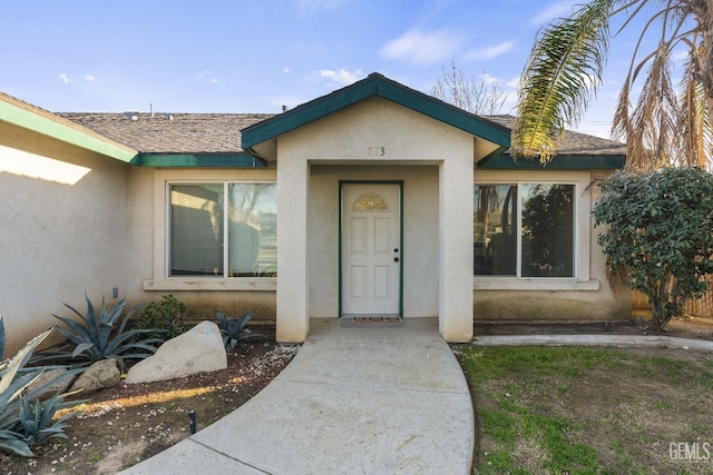 property entrance featuring roof with shingles and stucco siding