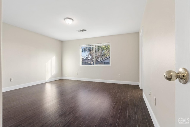 empty room with baseboards, visible vents, and dark wood-type flooring