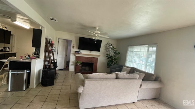 living area featuring light tile patterned floors, a fireplace, visible vents, and ceiling fan