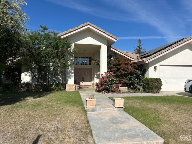 view of front facade with solar panels, a tile roof, a front yard, and stucco siding