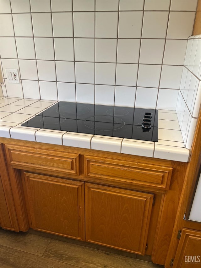 kitchen featuring decorative backsplash, black electric stovetop, brown cabinetry, and tile countertops