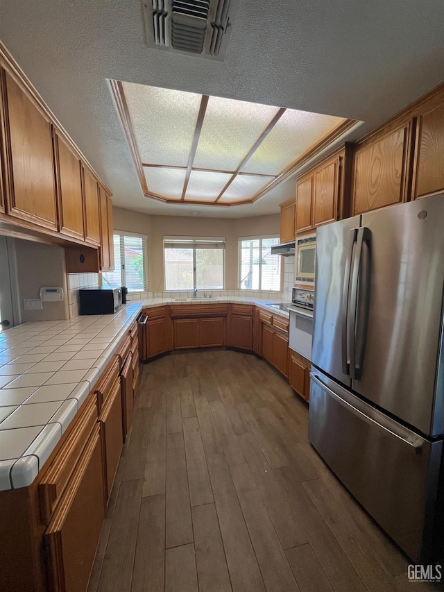 kitchen featuring stainless steel appliances, visible vents, tile countertops, brown cabinetry, and dark wood-style flooring