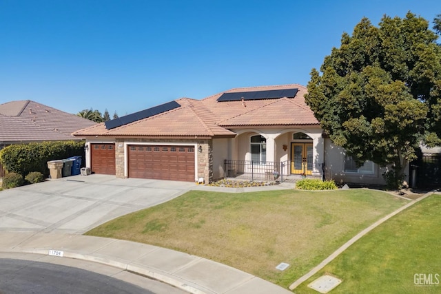 mediterranean / spanish home with a porch, an attached garage, solar panels, a tile roof, and a front yard