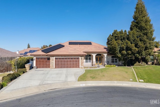 view of front of home with a tile roof, an attached garage, a front yard, roof mounted solar panels, and driveway