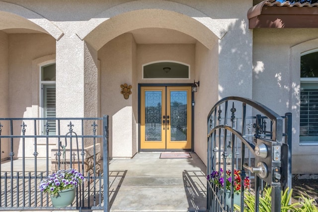 entrance to property featuring a tiled roof, a gate, french doors, and stucco siding