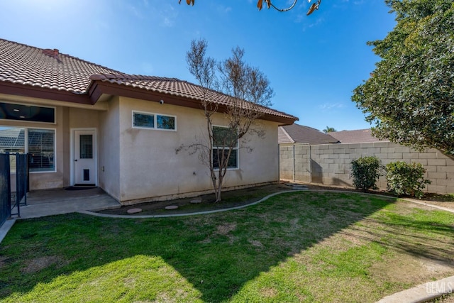 rear view of house featuring a tiled roof, a lawn, a fenced backyard, and stucco siding