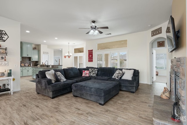 living room with arched walkways, recessed lighting, ceiling fan with notable chandelier, a fireplace, and light wood-style floors