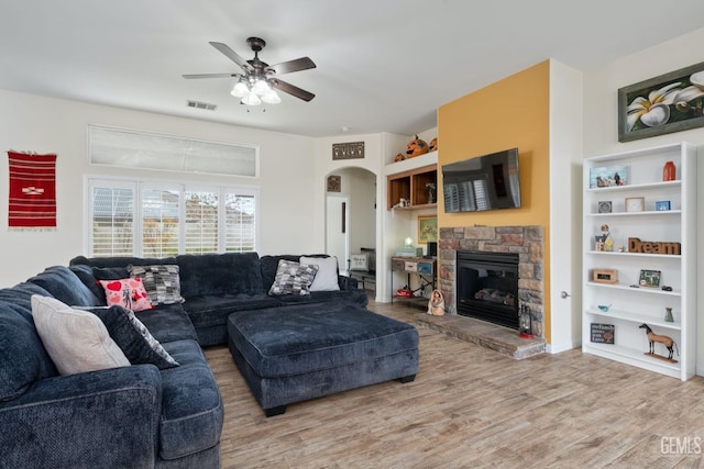 living area featuring arched walkways, ceiling fan, a stone fireplace, wood finished floors, and visible vents