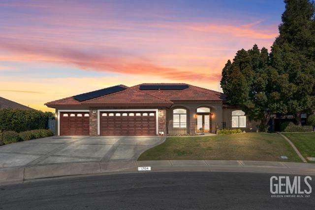 mediterranean / spanish-style home with a garage, concrete driveway, a front lawn, and a tile roof