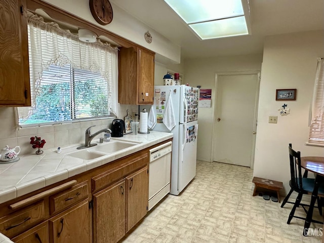 kitchen with tile counters, backsplash, brown cabinetry, a sink, and white appliances