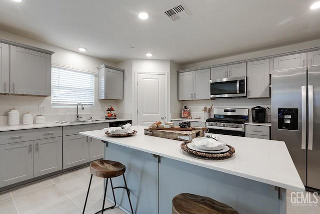 kitchen featuring a kitchen island, a kitchen bar, stainless steel appliances, sink, and gray cabinets