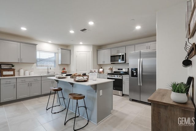 kitchen with sink, gray cabinets, a breakfast bar, a kitchen island, and stainless steel appliances