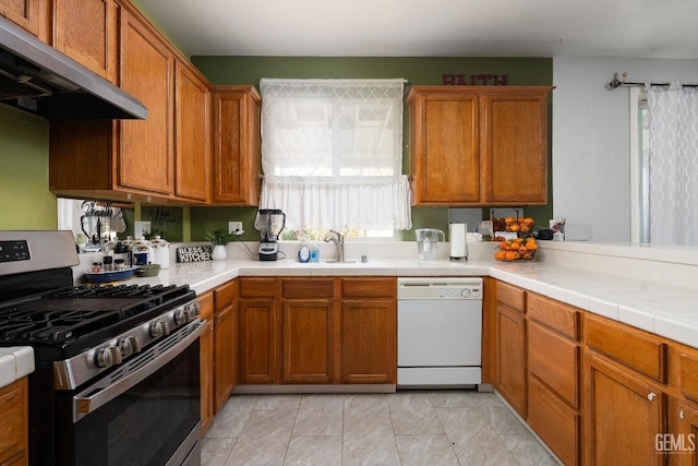 kitchen with exhaust hood, dishwasher, stainless steel gas range, sink, and tile countertops