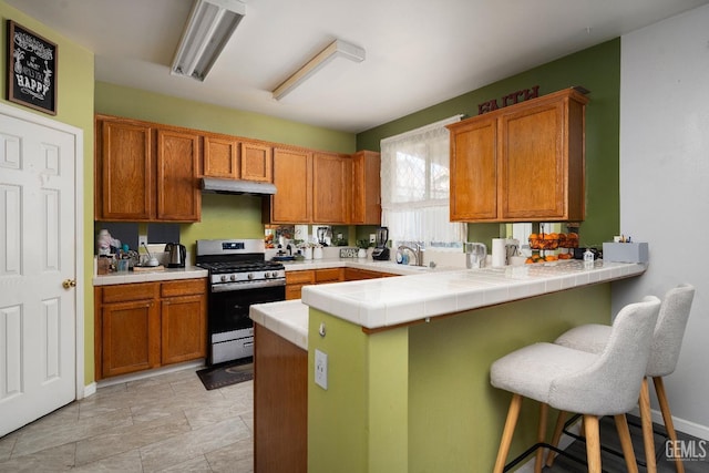 kitchen featuring kitchen peninsula, a kitchen breakfast bar, sink, stainless steel gas range oven, and tile countertops