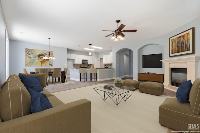 11311 Mezzadro Ave, Bakersfield, CA 93312 - living area featuring a glass covered fireplace, light wood finished floors, a ceiling fan, arched walkways, and a chandelier