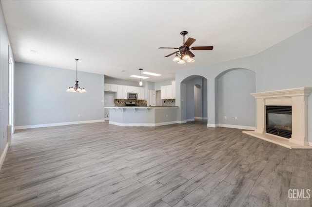 11311 Mezzadro Ave, Bakersfield, CA 93312 - unfurnished living room featuring a glass covered fireplace, ceiling fan, light wood-style floors, arched walkways, and a chandelier